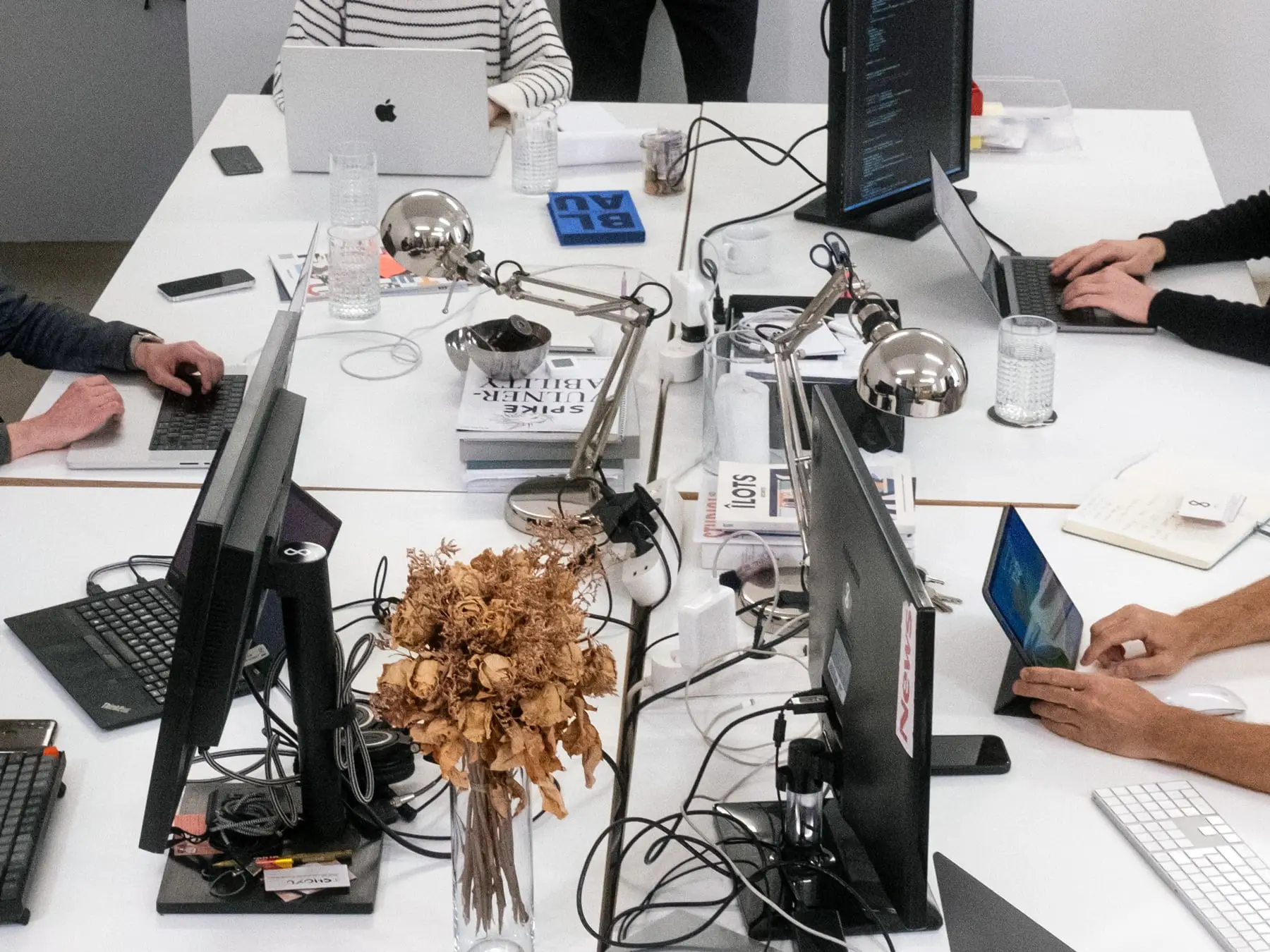 A busy table at the pagestrip office, full of Macbooks, cables, papers, and magazine, with hands visible from all sides of the table.